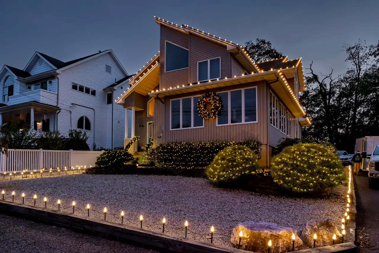 Two-story home with warm white roofline holiday lights and a lit walkway at dusk